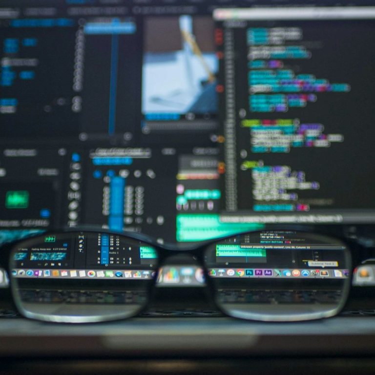 Glasses resting on a computer keyboard displaying coding and editing software.