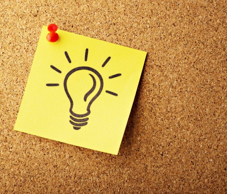 A light bulb illustration on a yellow sticky note pinned to a corkboard.