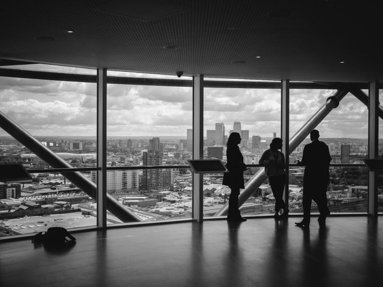 Silhouettes of three people viewing a city skyline through large windows.