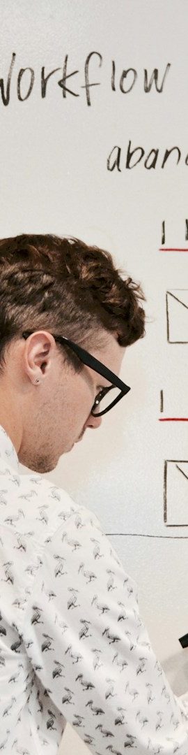 Person writing on a whiteboard with a diagram and notes about workflow processes.