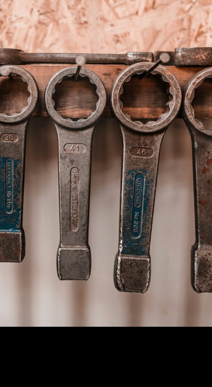 Five metal wrenches hanging on a wooden surface, showcasing their various sizes.